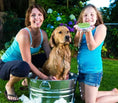 Load image into Gallery viewer, Woman and girl grooming a golden retriever in a tub outdoors, using a Comfort Pet Grooming Brush for a fun bath time.
