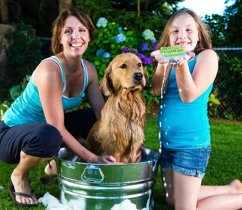 Woman and girl grooming a golden retriever in a tub outdoors, using a Comfort Pet Grooming Brush for a fun bath time.